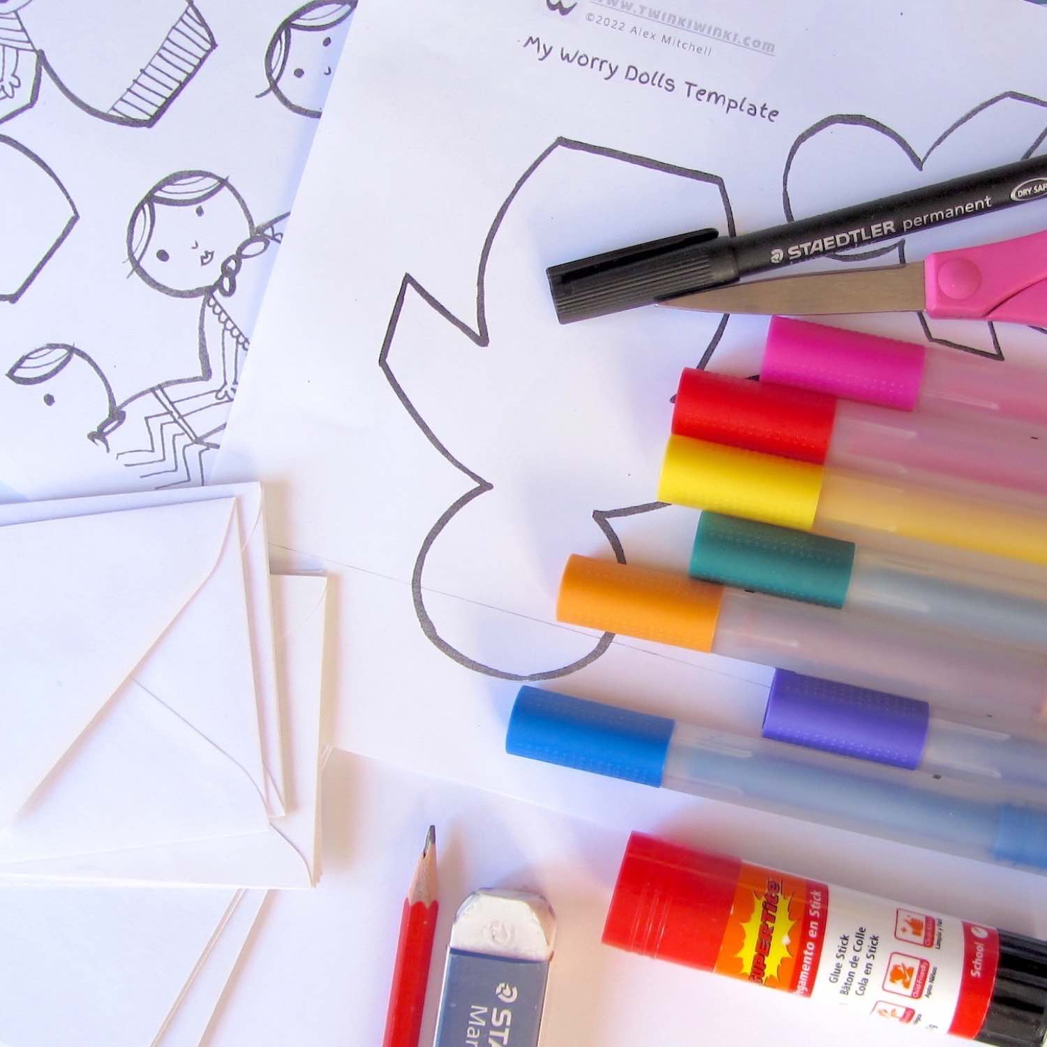 Colorful markers, a pencil, eraser, scissors, and glue stick on top of coloring pages and stacks of white envelopes.