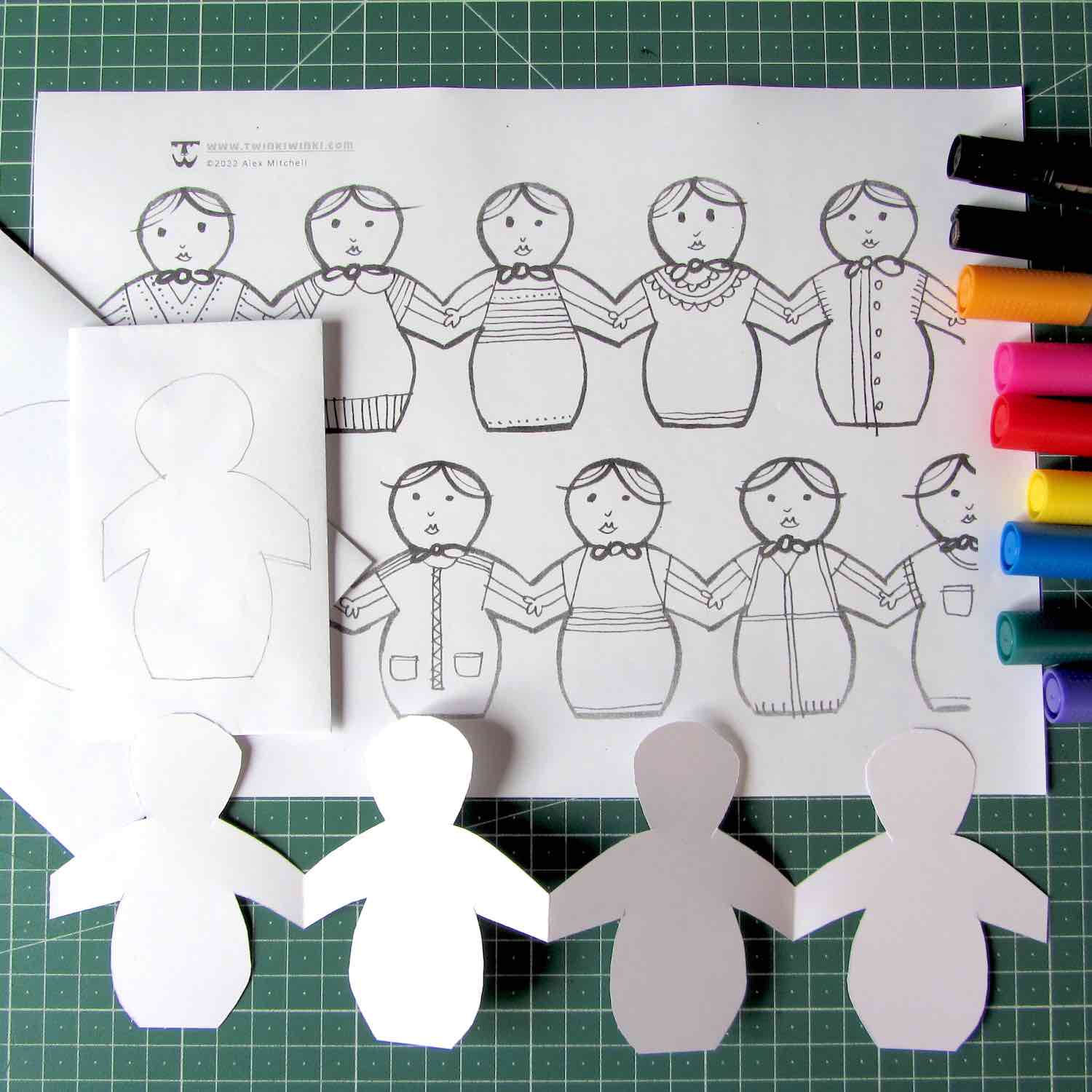 White envelopes and a paper doll chain on top of a cute coloring page with colorful markers on the right.