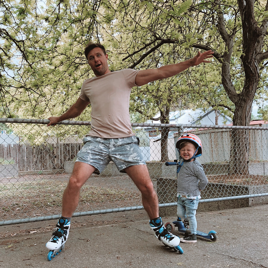 Funny dad on inline skates with toddler riding 3 wheel scooter