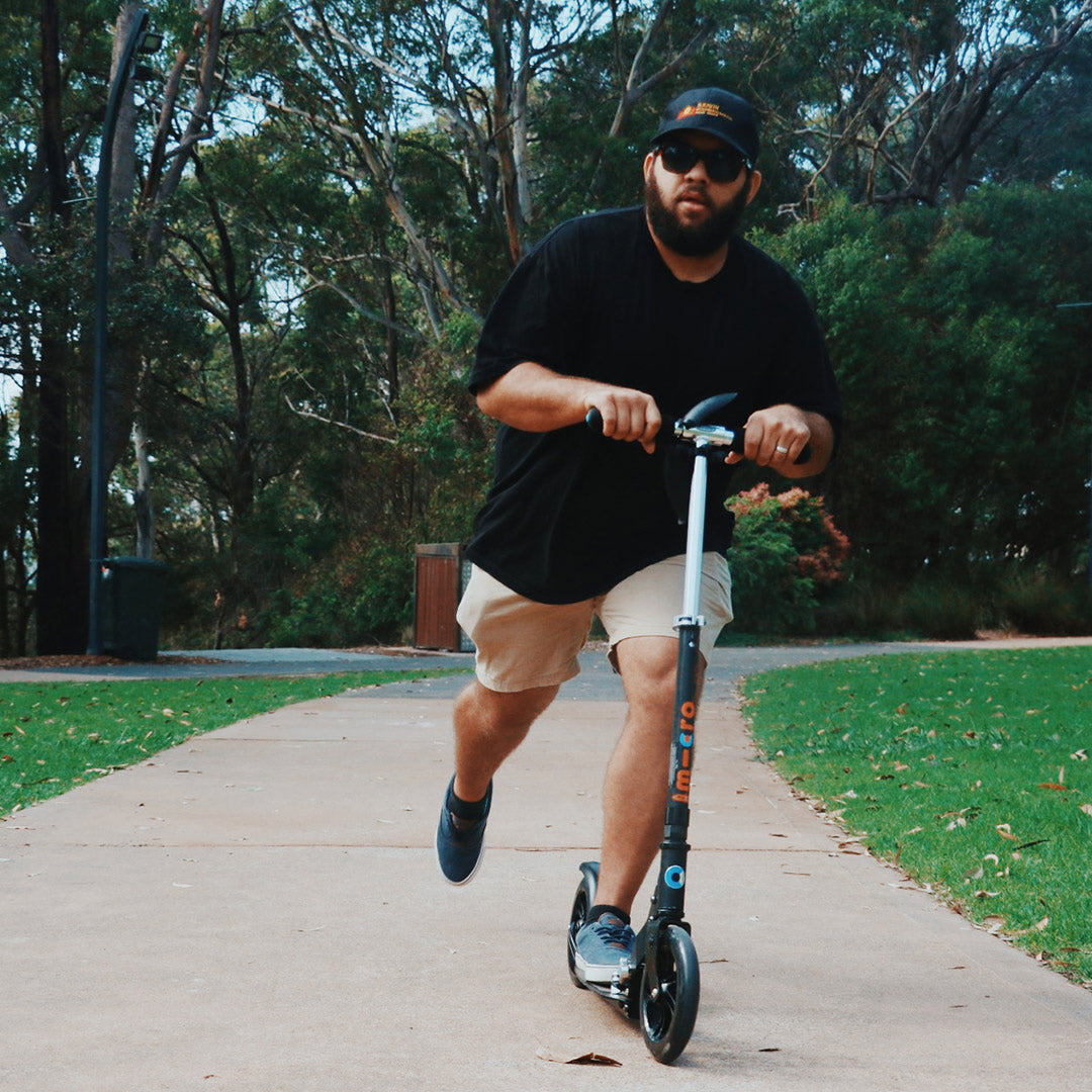 Dad riding an adult Micro Scooter through the park