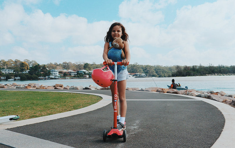 girl riding a maxi micro deluxe 3 wheel scooter by beach