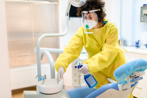 A female dental assistant using a blue surface disinfectant and cleaner in dental setting.
