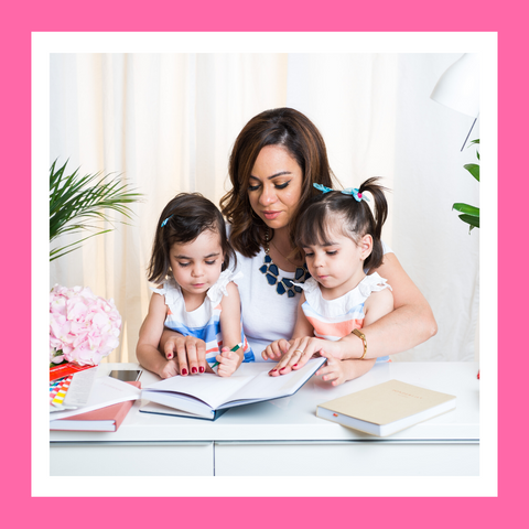 woman holding books and sitting at a desk with her twin daughters