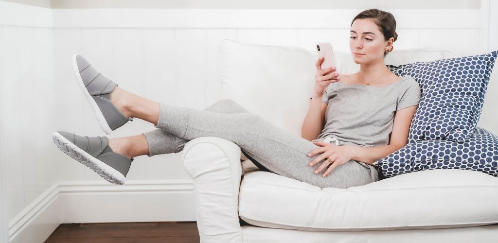 A woman in Zenz shoes sitting on a couch looking at a phone