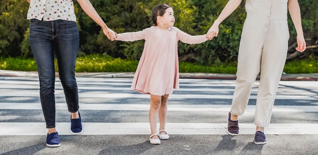 Two adults and a little girl holding hands as they cross the street wearing Zenz shoes