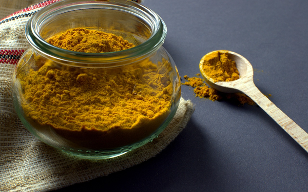 A glass jar and wooden spoon full of turmeric powder.