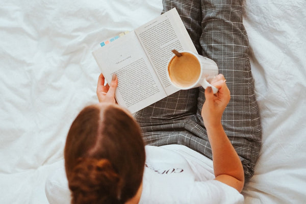 a woman reading a book and drinking coffee