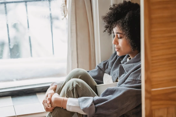 A young woman sitting in the corner with a box of tissues