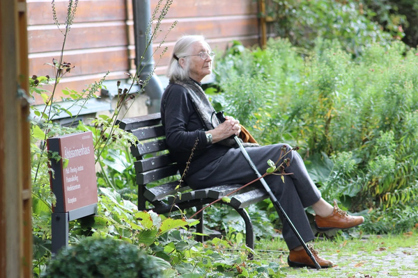  A senior woman with a cane sitting on a bench outside