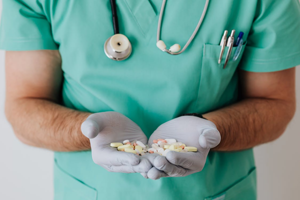 A doctor in mint scrubs holding a handful of vitamins and supplements