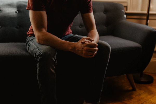 A man sitting on a gray couch with his arms on his knees