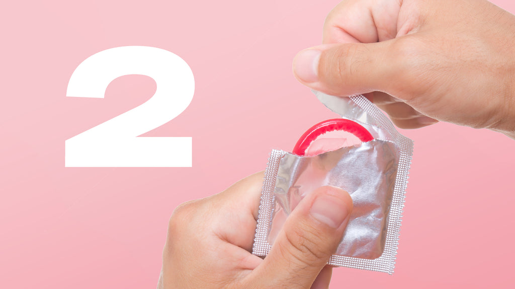 Des mains ouvrant un emballage de condom avec le chiffre 2 écrit en blanc à côté. 