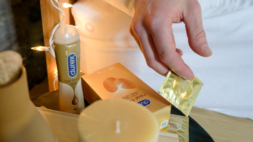 Main saisissant un condom Durex Real Feel naturel sans latex, à côté d’une bouteille de lubrifiant Durex Real Feel.
