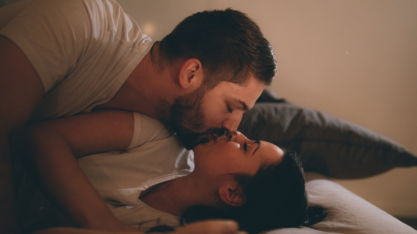 Two people sharing a kiss while in bed together.