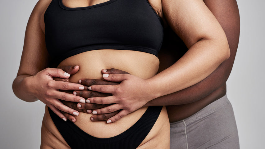 Man holding his partner’s stomach from behind while her hands rest on top of his.