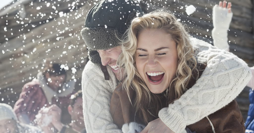 Man surprising a woman with a hug from behind on a snowy day.