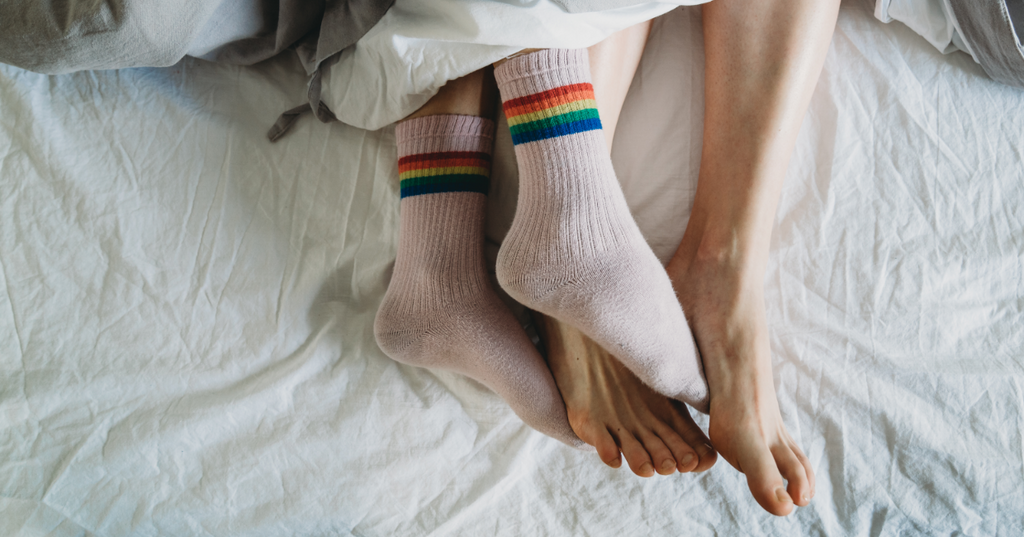 Person wearing socks rubbing the feet of their partner in bed.