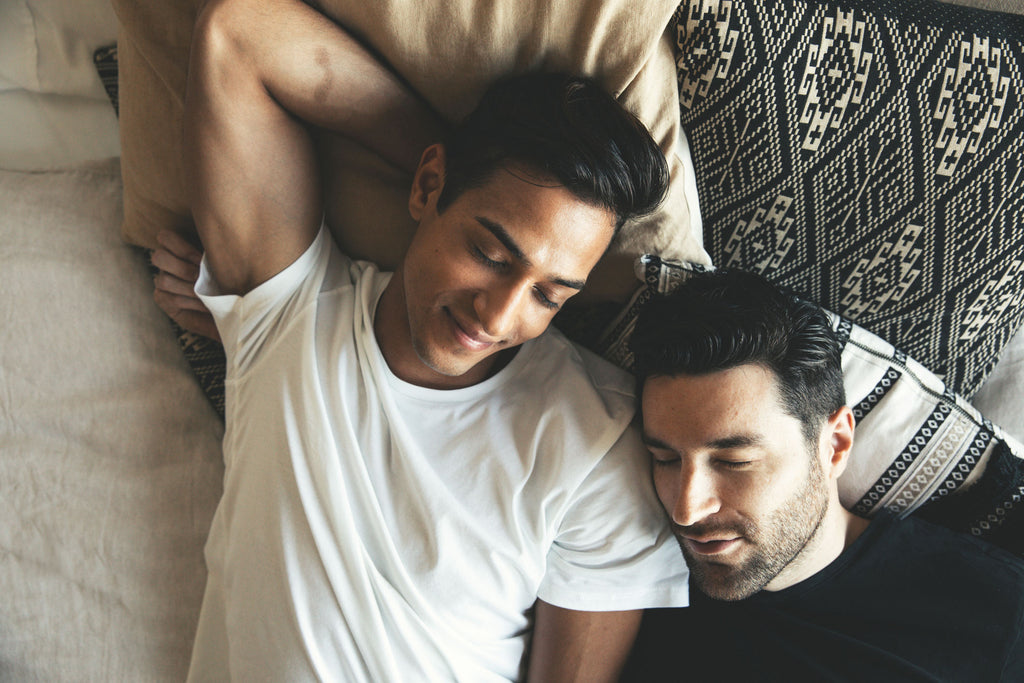 Two men laying nestled next to each other in bed.