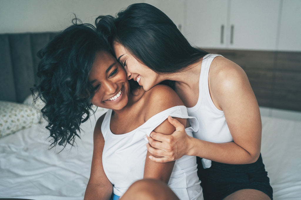 Deux femmes souriant tout en se caressant au lit.