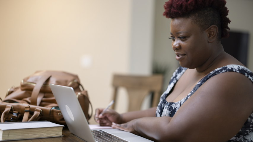 Woman browsing her laptop while taking notes on a piece of paper.