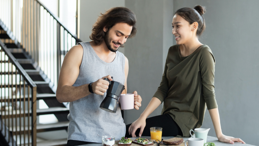 Two people enjoying a cup of coffee and orange juice in casual clothing in their kitchen.