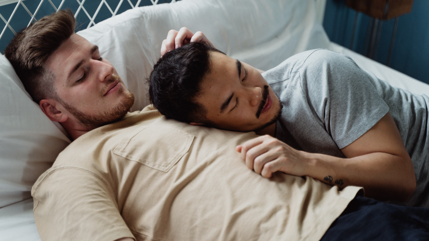 Un homme, la tête couchée sur la poitrine de son partenaire dans un lit. 