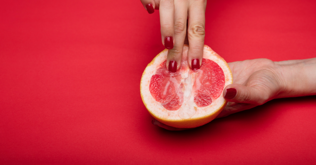 Two fingers pressing down on an open grapefruit, signifying the act of fingering.