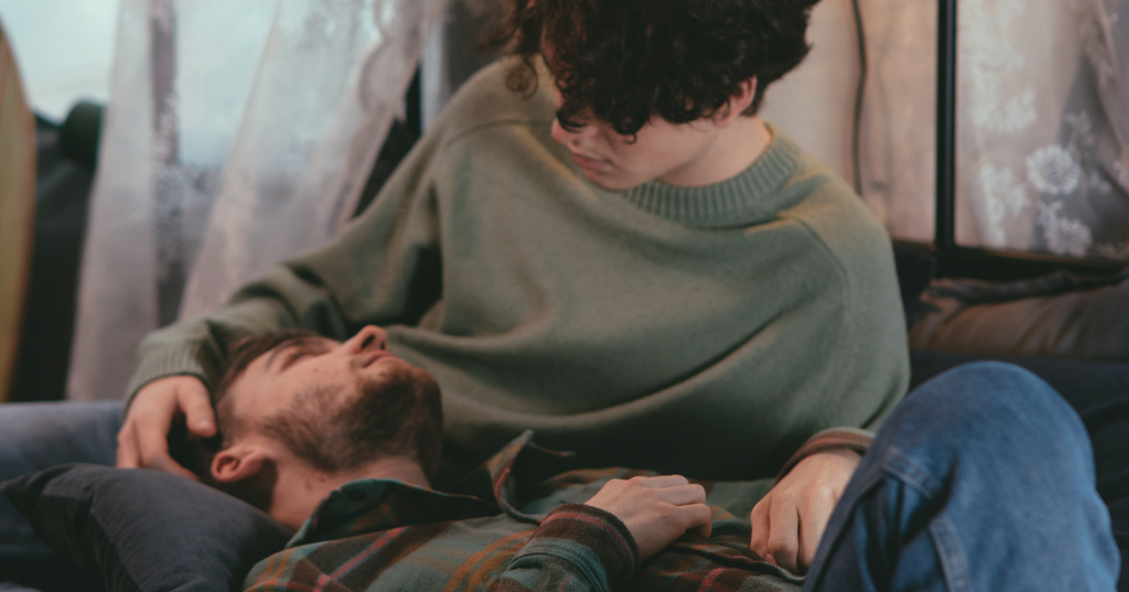 Man laying on the lap of his partner while gazing into his eyes.