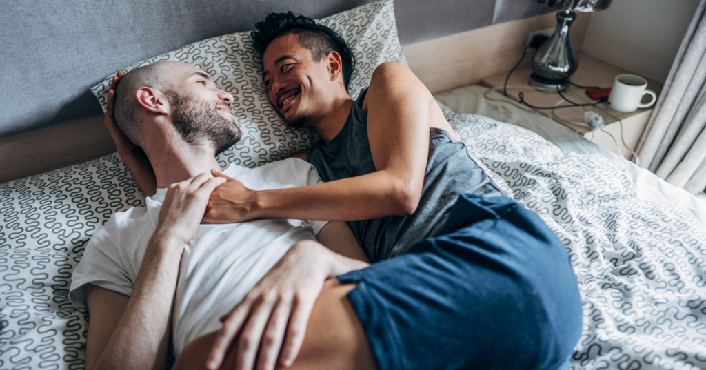 Two men cuddling up to one another in bed.