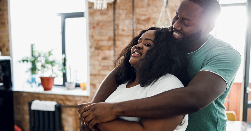 Man lovingly draping his arms around his girlfriend.