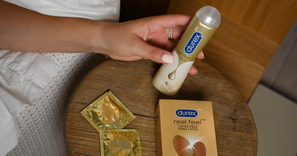 Hand reaching for Durex<sup>®</sup> Real Feel Pleasure Gel on a table beside Durex condoms.