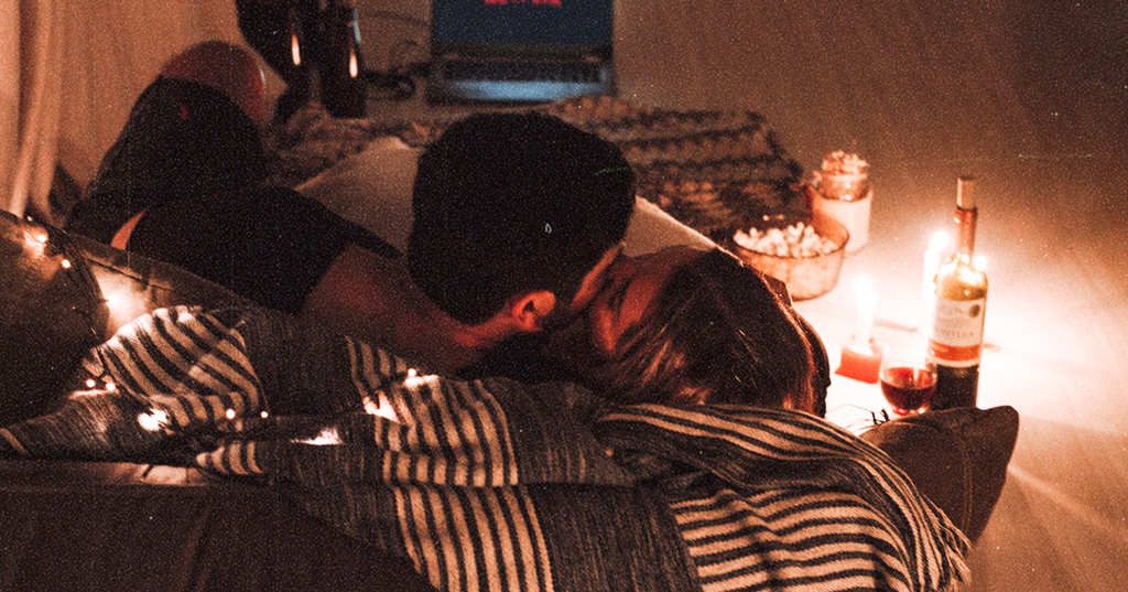 A couple softly kissing in bed before intimate sex takes place.