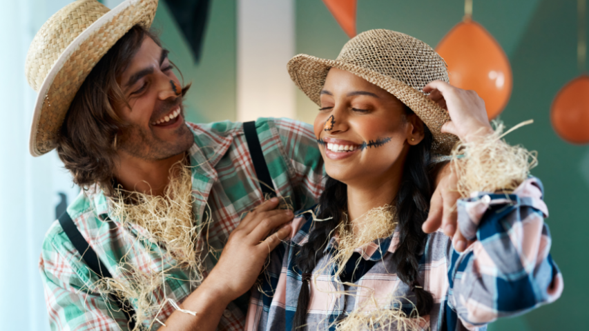 Man and woman dressed as scarecrows laughing together at a Halloween party.