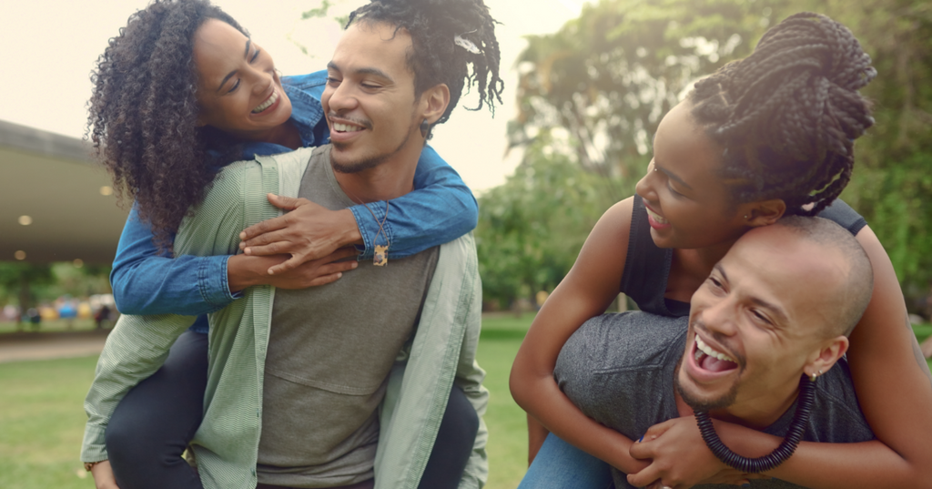 Two women on their partner’s backs sharing a laugh.