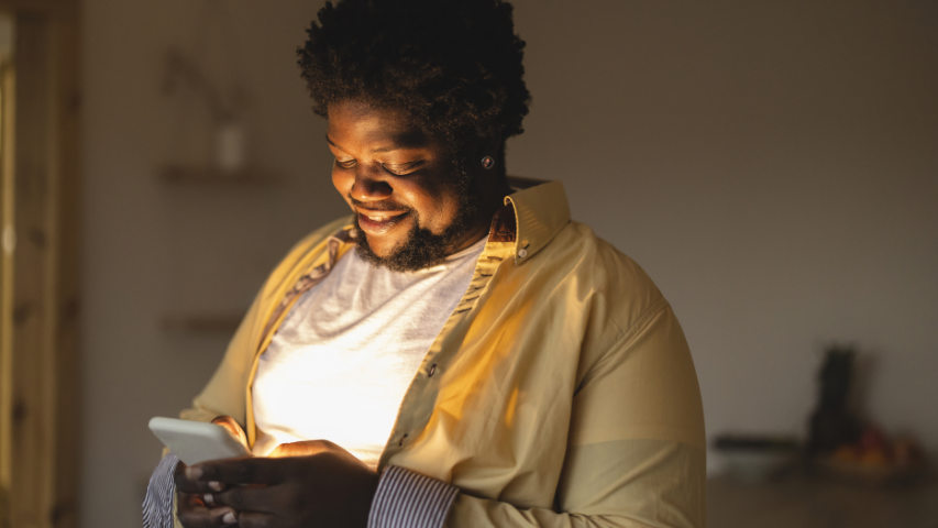 Man smiling while his face lights up from his phone screen.