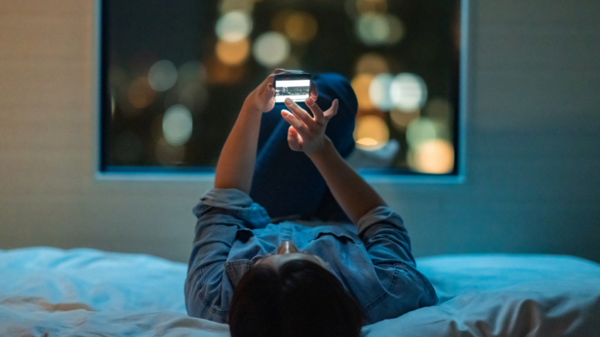 Person laying on their bed while holding their phone above them.