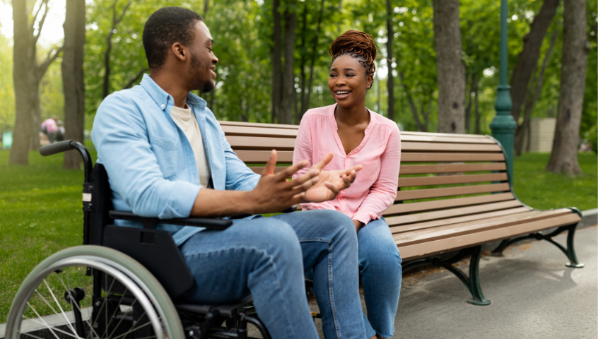 Man in wheelchair candidly explaining situationships to a woman on a bench.