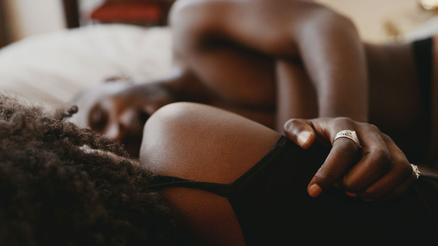 Un homme torse nu qui pose sa main sur le dos de sa partenaire alors qu’ils sont étendus côte à côte dans un lit.