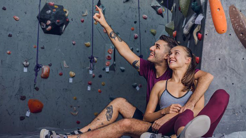 Happy couple pointing at rock climbing walls while smiling on a date.