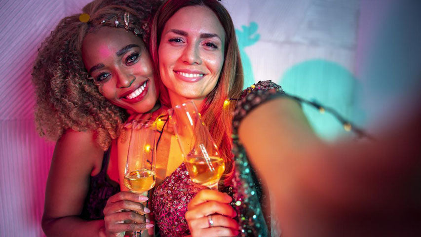 Une femme qui tient un appareil photo tout en levant son verre de champagne avec sa partenaire.