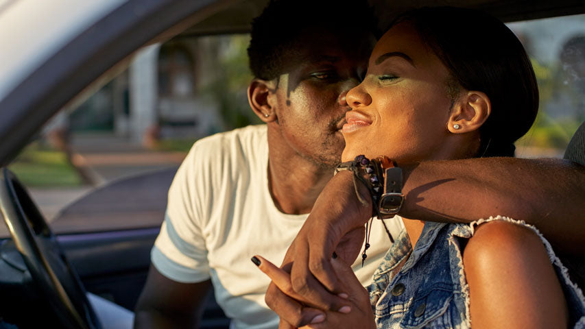 Man wrapping his arm around his partner while interlocking hands and kissing her cheek in the car.