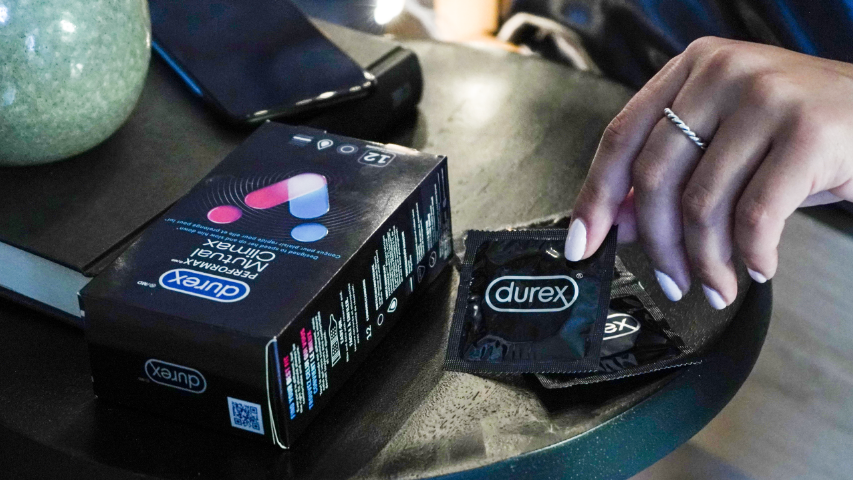 Une main qui saisit un condom Durex Mutual Climax sur une table de chevet.