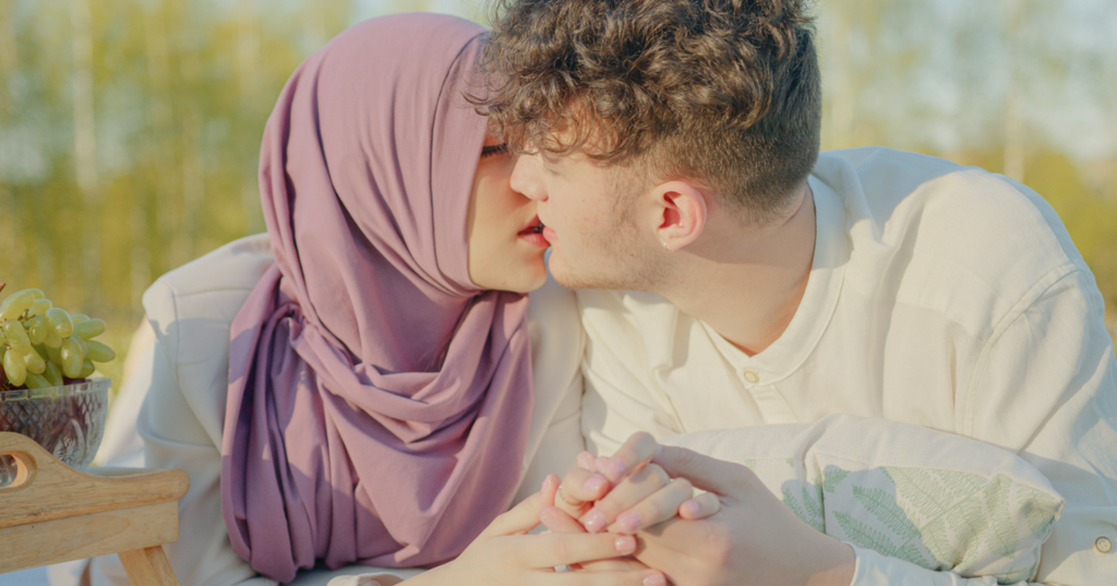 Woman in a purple hijab kisses her partner while holding his hand.