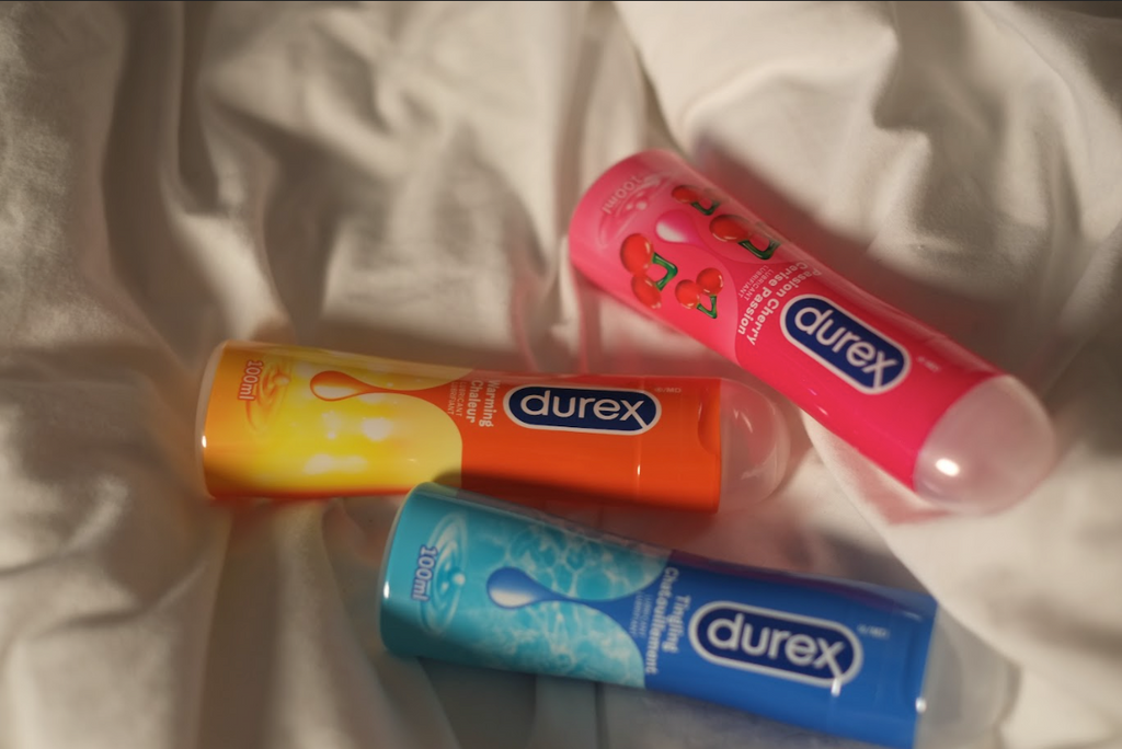 Durex Original, Durex Warming, and Durex Passion Cherry lube bottles on bedsheets.