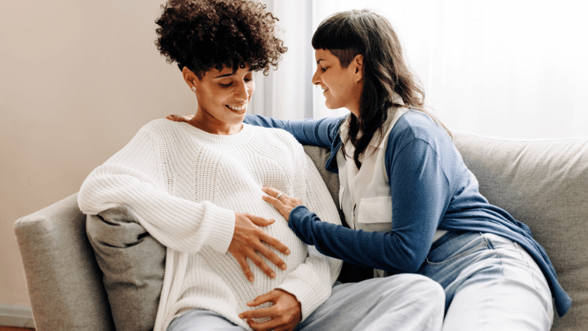 Woman with baby bump rubs her belly alongside her partner.