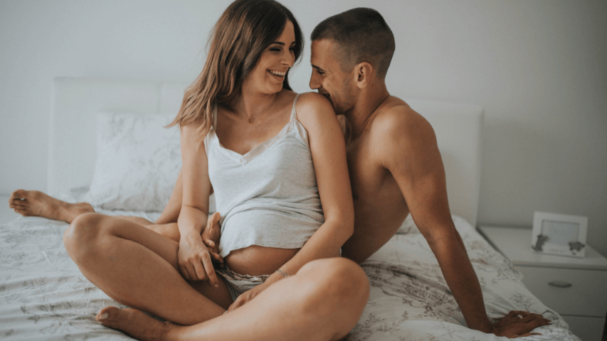 Couple smiling in bed together while expecting a baby’s arrival.