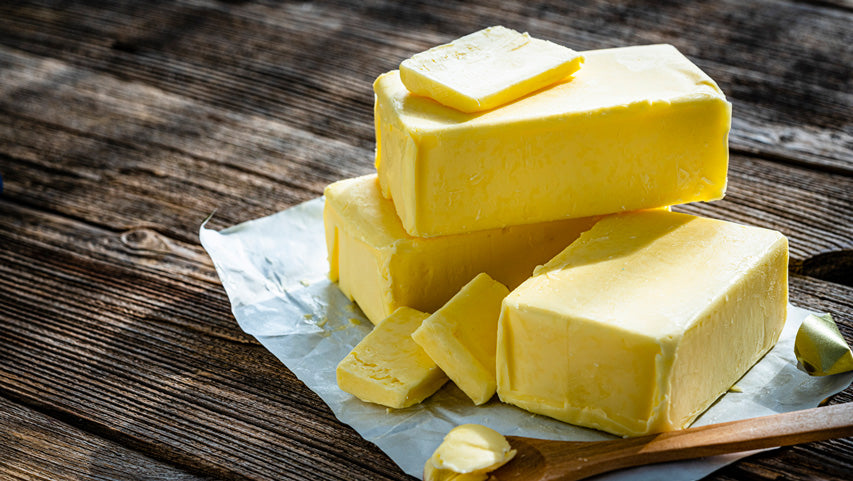 Three sticks of butter on top of a wrapper next to a wooden spoon sit on a wooden deck.