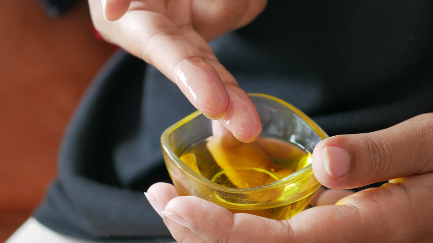 Two fingers dabbing into a small dish filled with olive oil.
