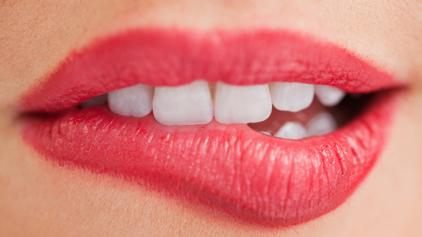 Une personne portant du rouge à lèvres rose se mord la lèvre.