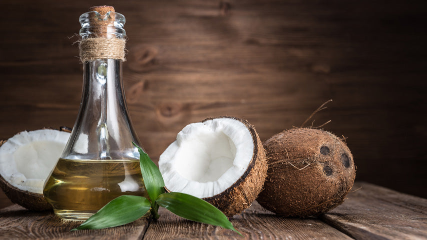 Freshly cracked open coconut displayed next to another coconut and a fancy bottle of coconut oil.